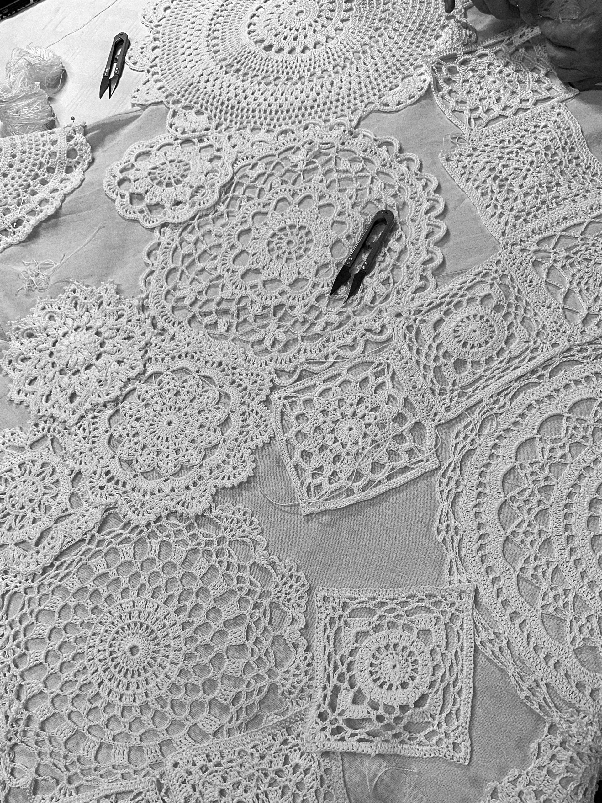 Overlaid layout of intricate white lace doilies hand-crocheted motifs on a workspace table during development of a custom gown for Polo Ralph Lauren